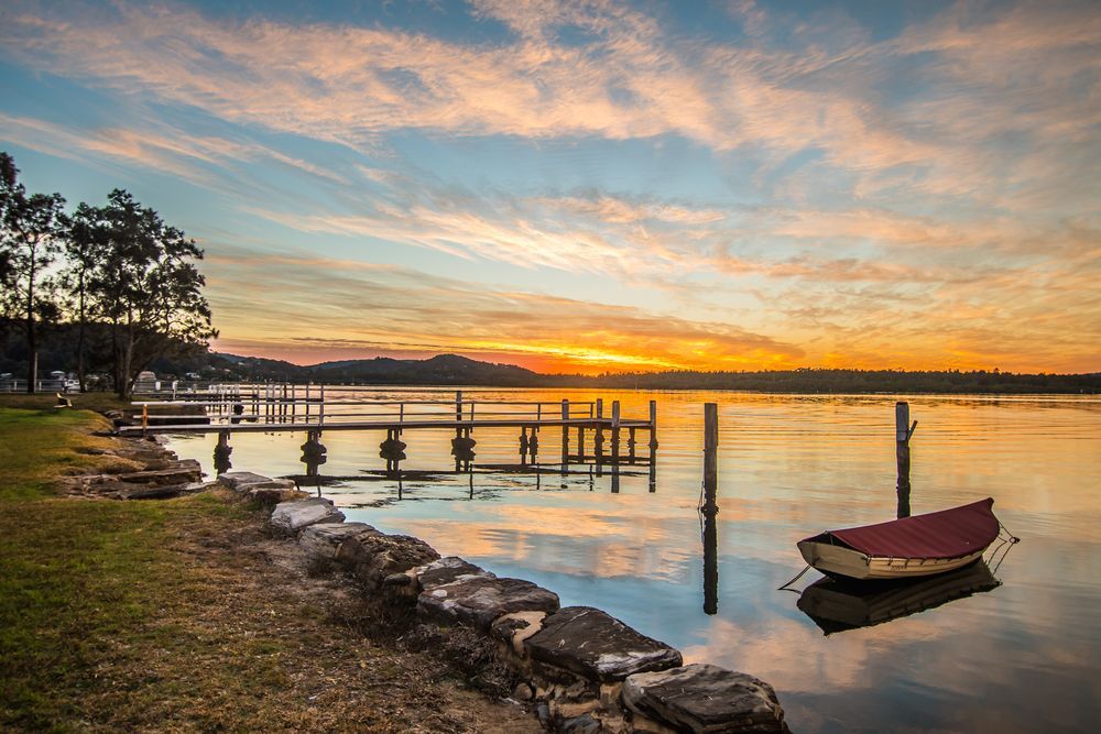 A Boat Is Floating On The Water Near A Dock At Sunset — Roof & Guttering Solutions In Woy Woy, NSW