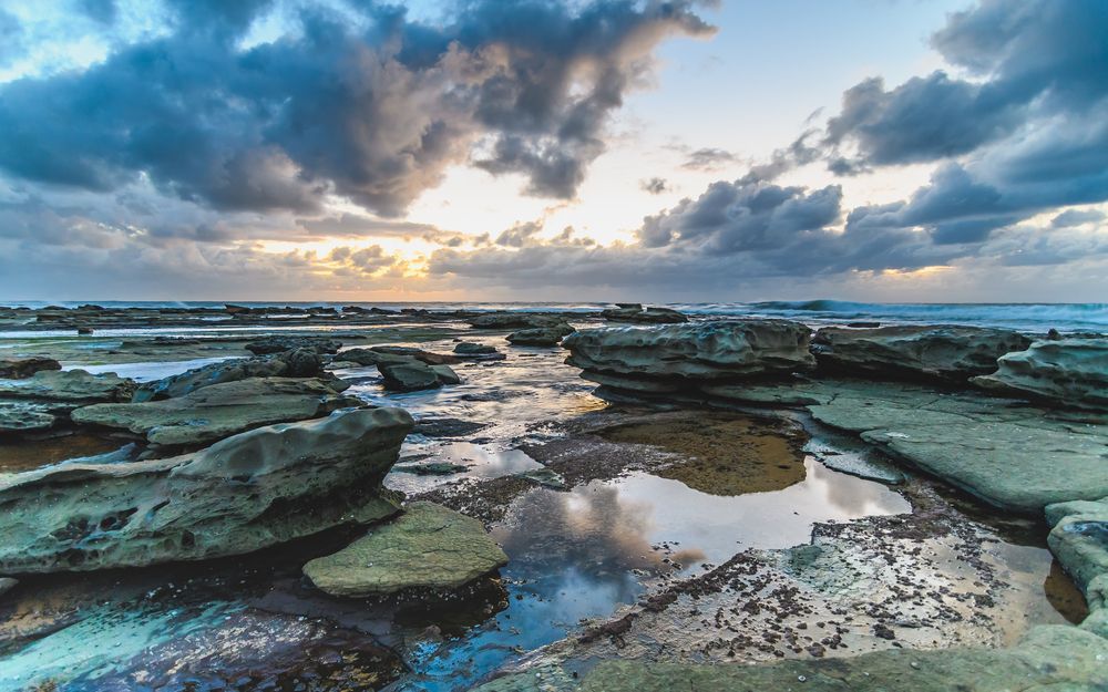 A Sunset Over A Rocky Beach With A Cloudy Sky — Roof & Guttering Solutions In Gosford, NSW