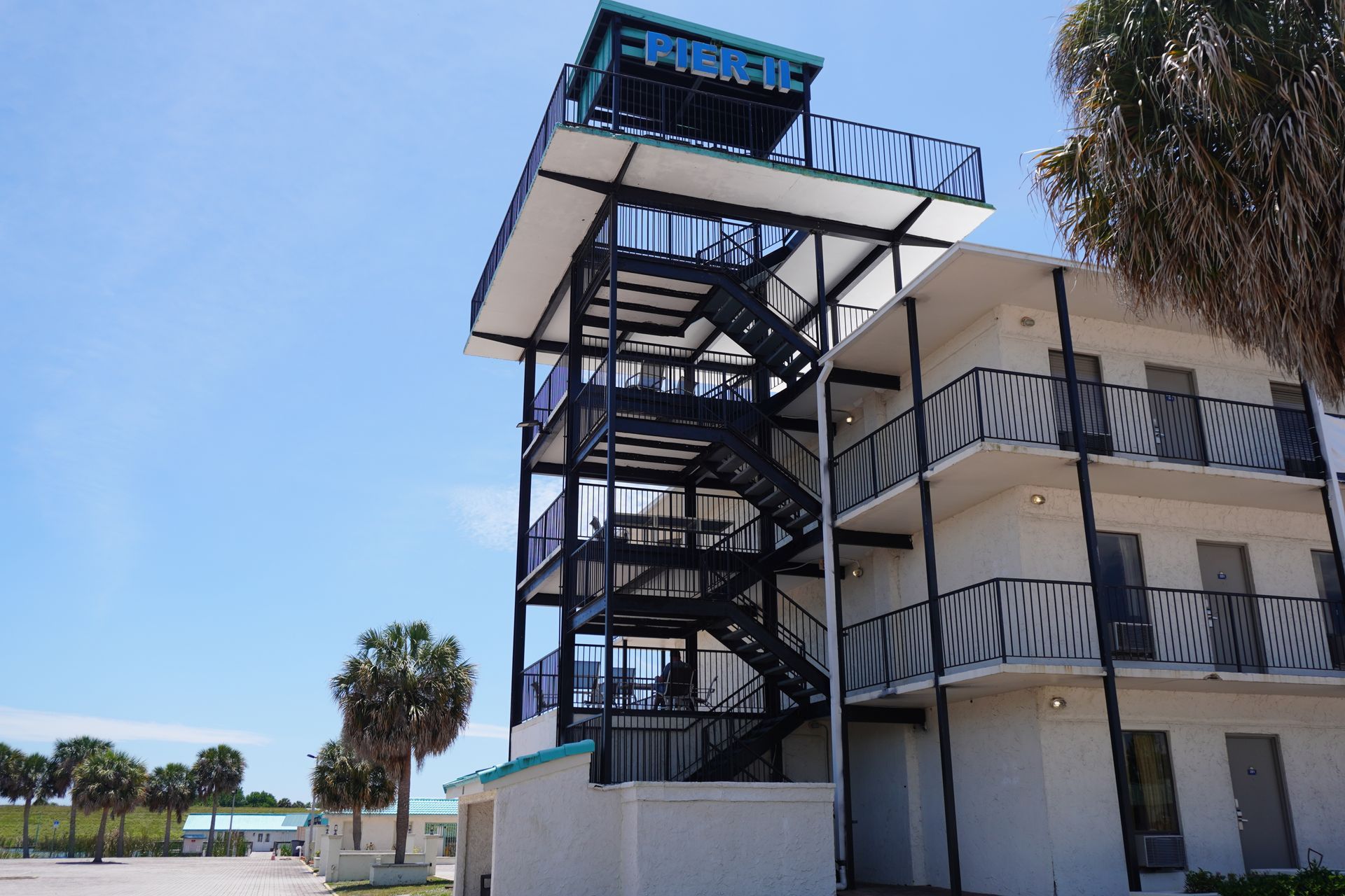 Outdoor staircase beside a beige building under a blue sky with palm trees nearby