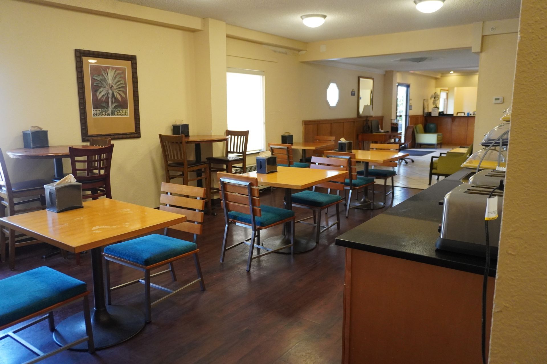 Empty restaurant dining area with wooden tables, blue chairs, and a serving counter