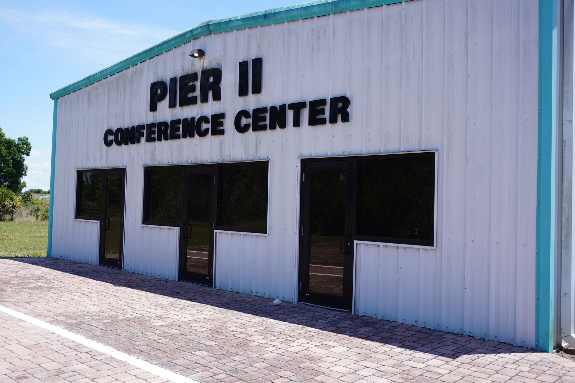 Pier II Conference Center building with white siding, teal trim, and dark windows on a sunny day