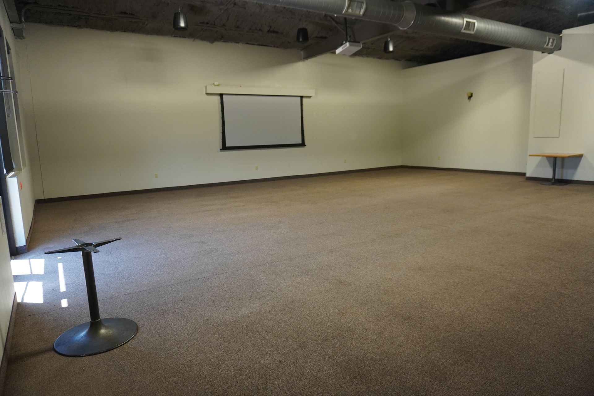 Empty carpeted conference room with projector screen and exposed ceiling pipes