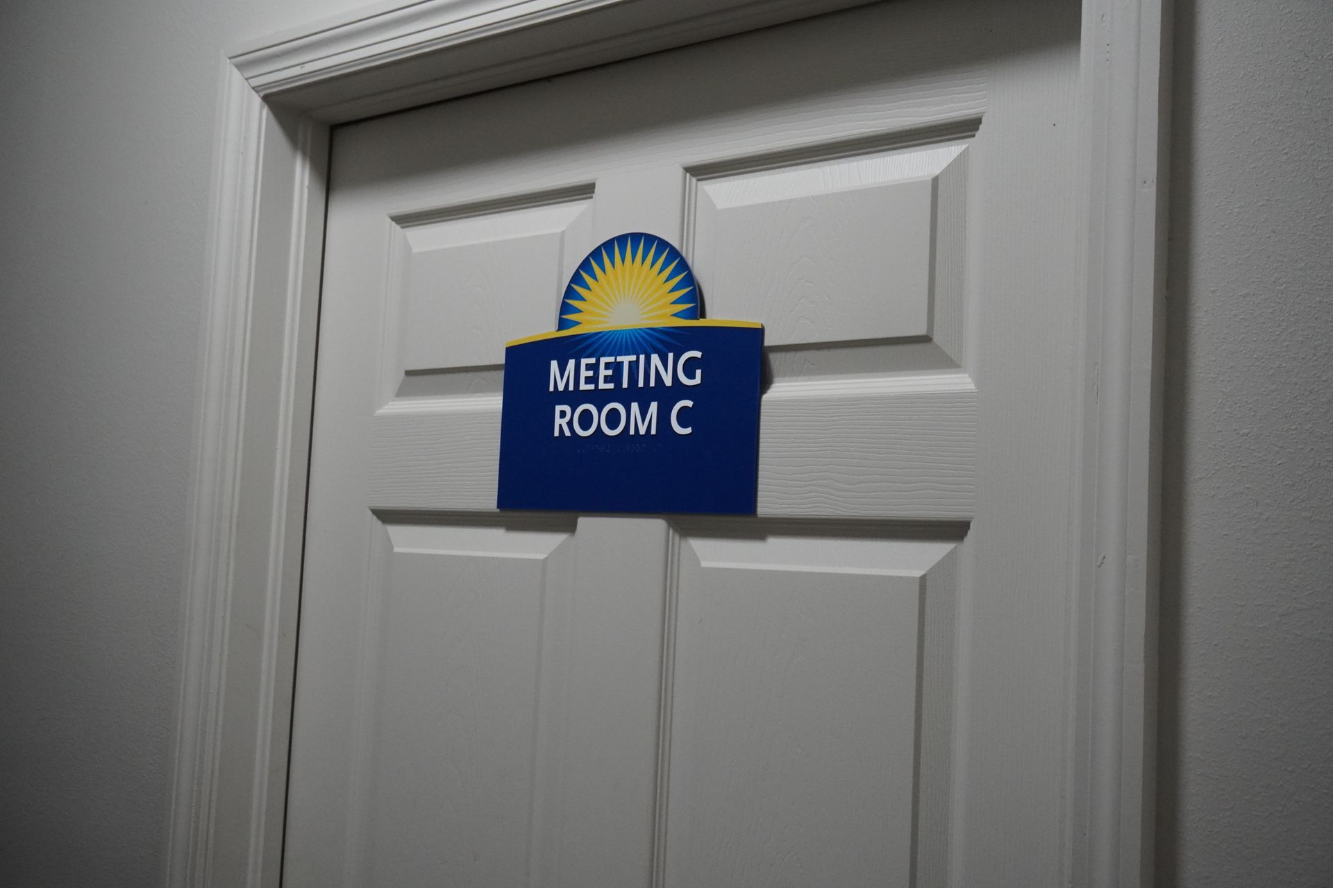 Blue sign reading “Meeting Room C” on a white door with a sunburst logo.