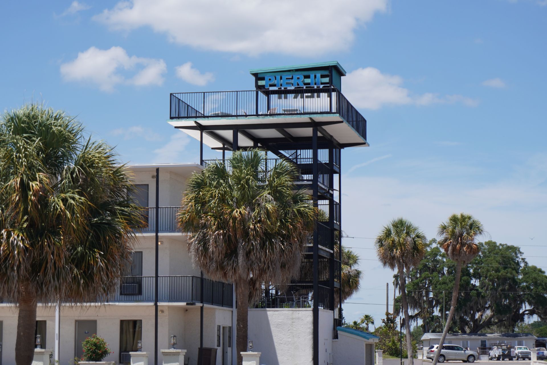 Motel building with palm trees and a rooftop neon sign under a blue sky