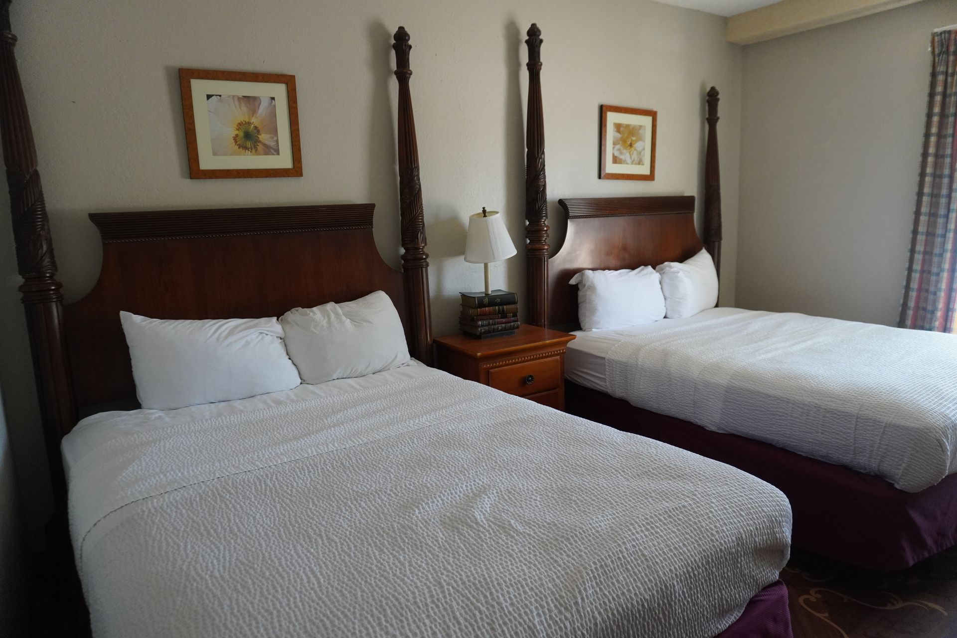 Hotel room with two made beds, white bedding, dark wooden headboards, and a bedside lamp between them