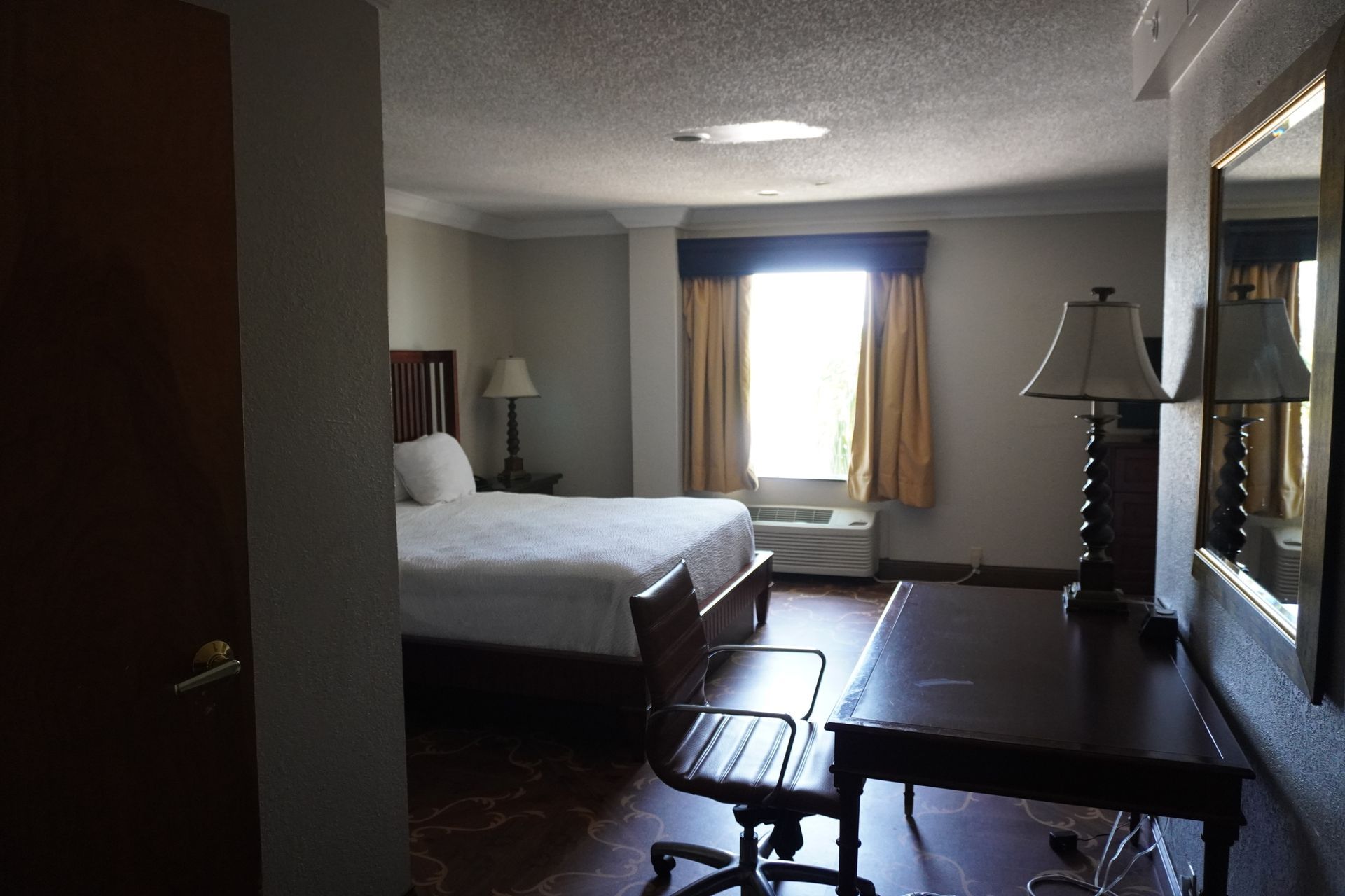 Hotel room with a bed, desk, lamp, and window with curtains