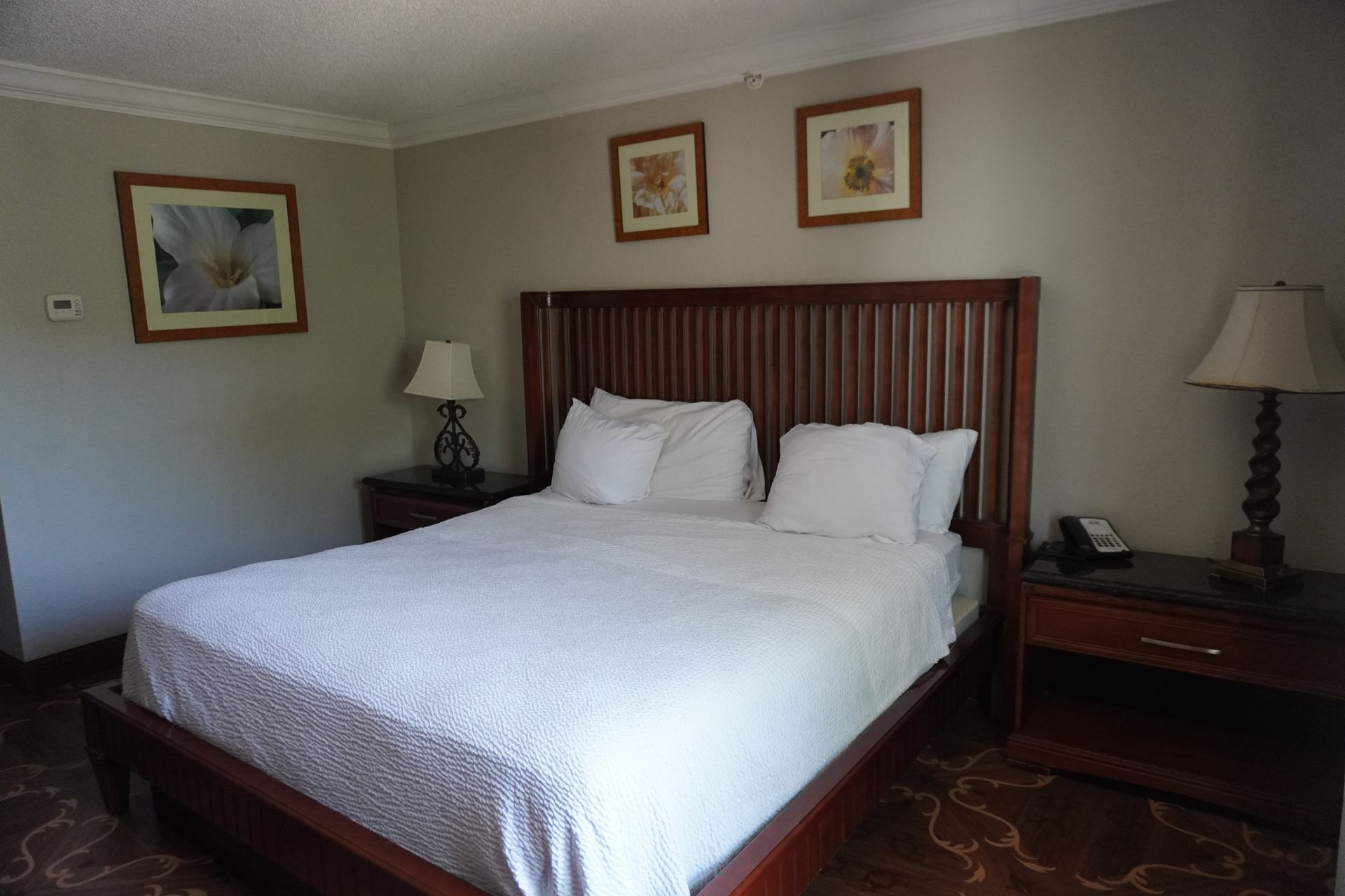 Neat bedroom with a large bed, white bedding, dark wood furniture, lamps, and framed wall art.