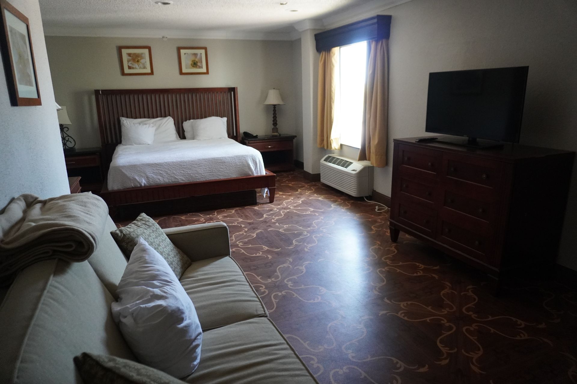 Hotel room with a bed, sofa, dresser, TV, and window with blue curtains