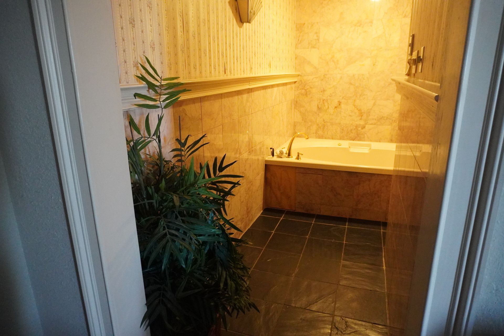 Small bathroom with beige tiled shower, dark floor tiles, and a potted plant near the doorway.