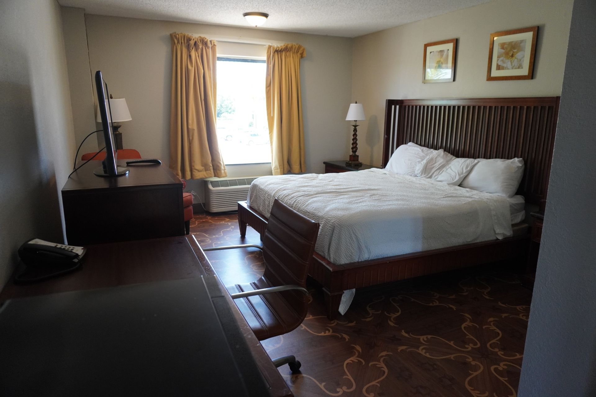 Bedroom with a large bed, dark wood furniture, and a bright window with curtains