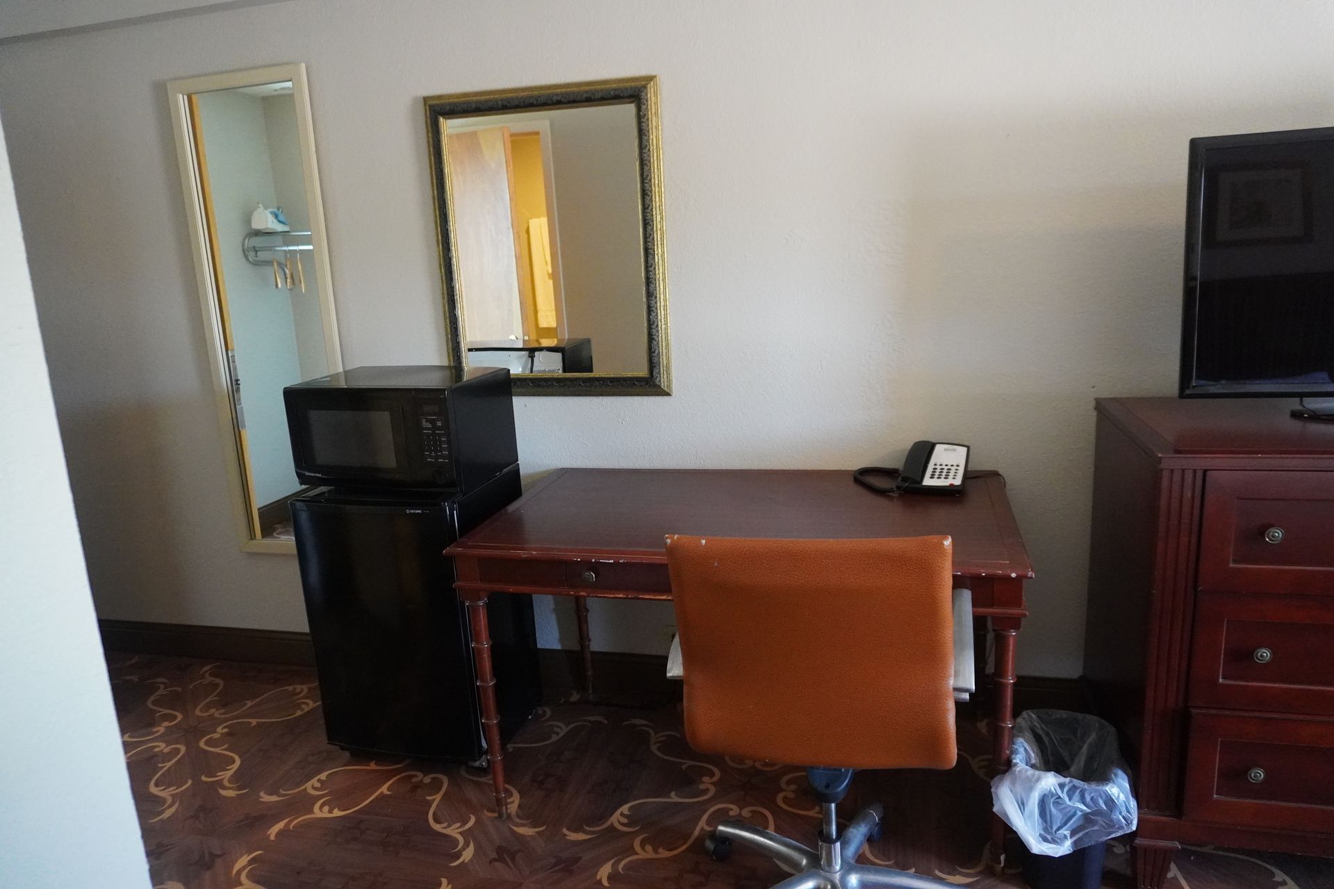 Hotel room with desk, chair, mini fridge, dresser, mirror, and TV