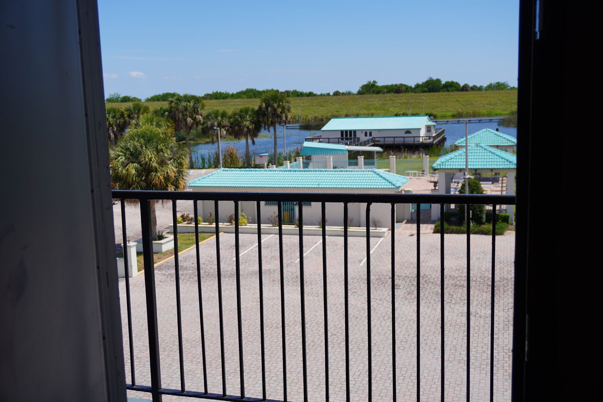 View from a balcony of a pool, cabana, and greenery under a clear blue sky