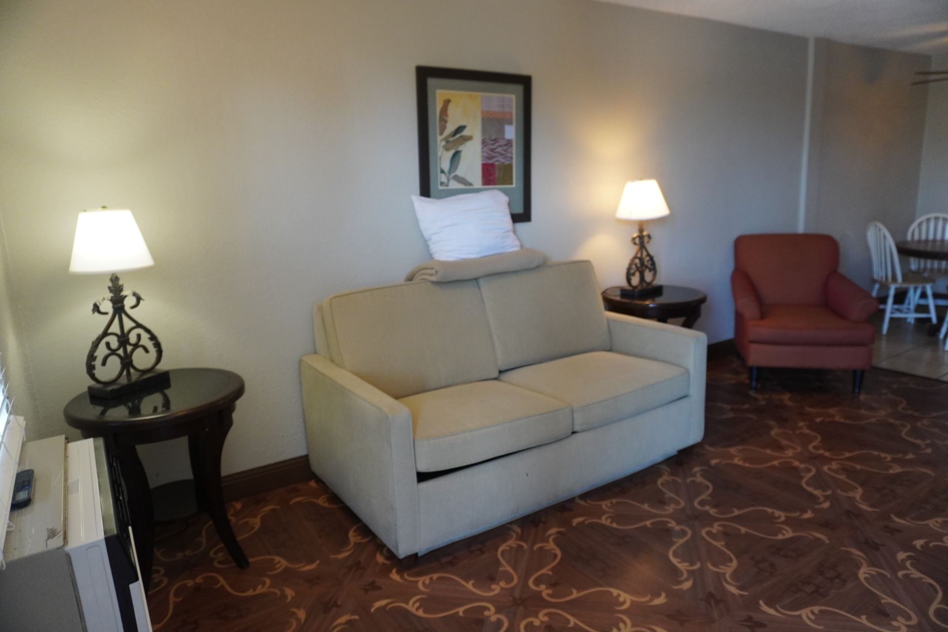 Hotel seating area with beige sofa, red armchair, two lamps, and patterned carpet