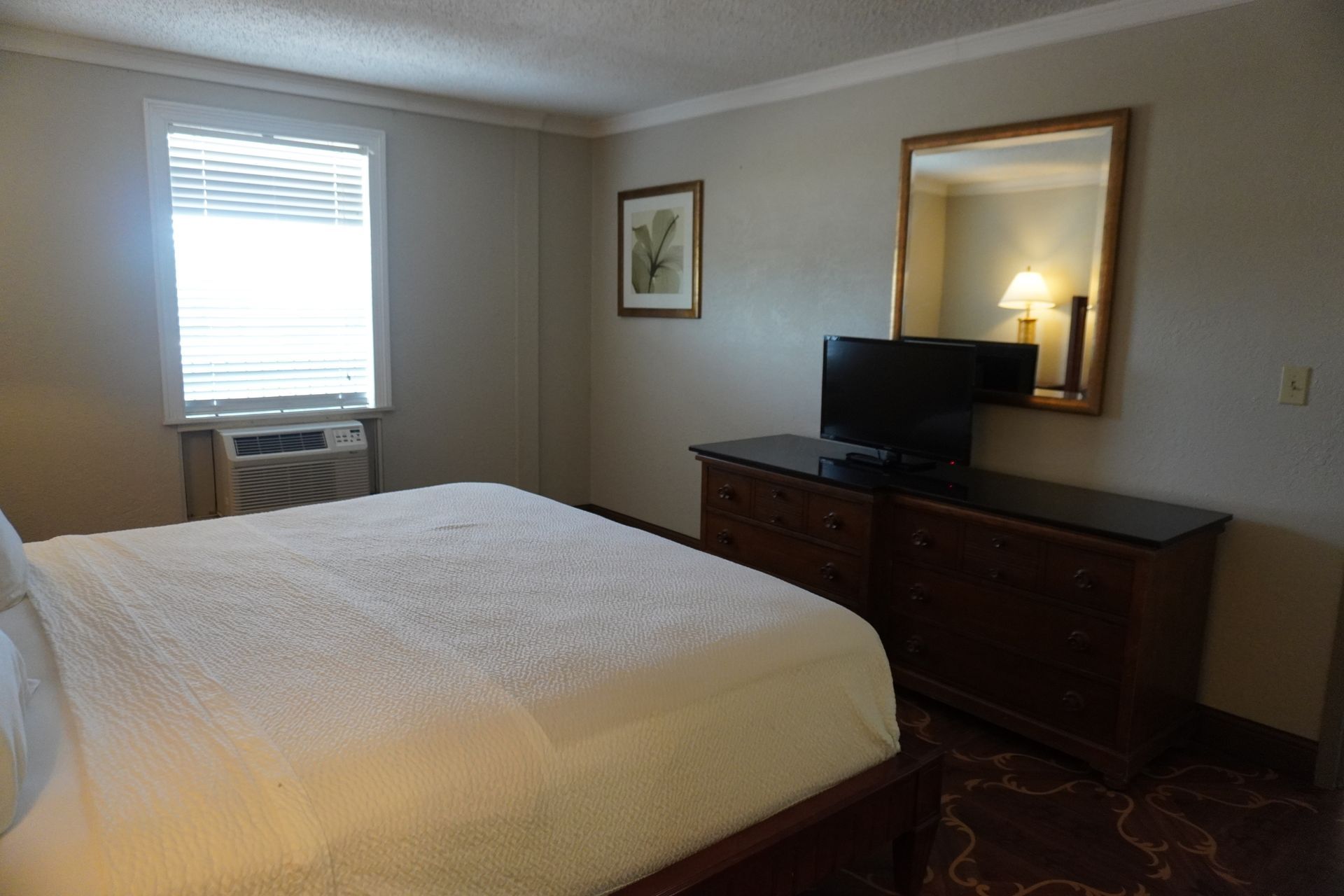 Bedroom with white bedspread, dresser with TV, window air conditioner, and framed wall art