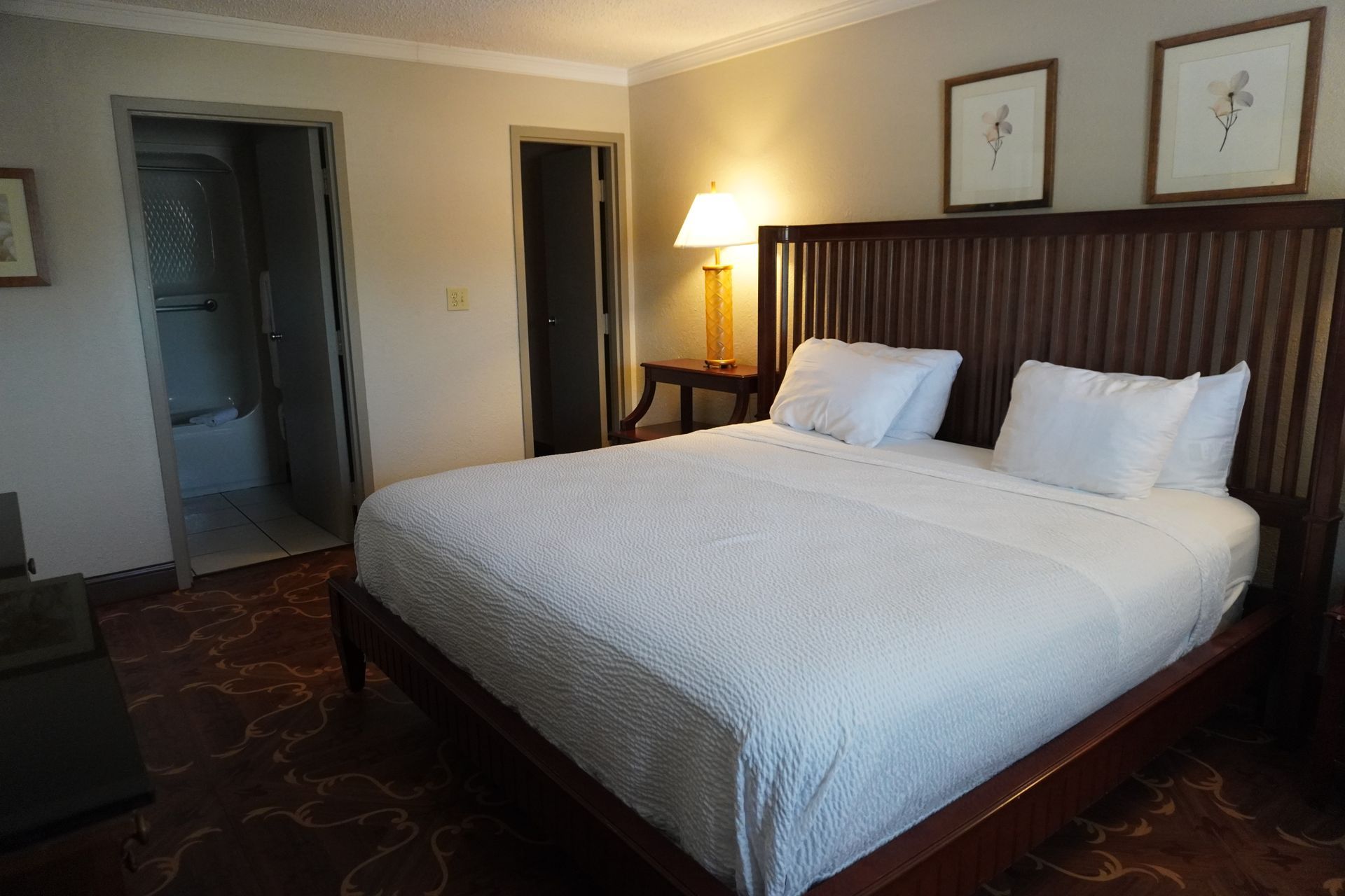 Cozy hotel room with a king bed, bedside lamp, and two framed pictures above the headboard.