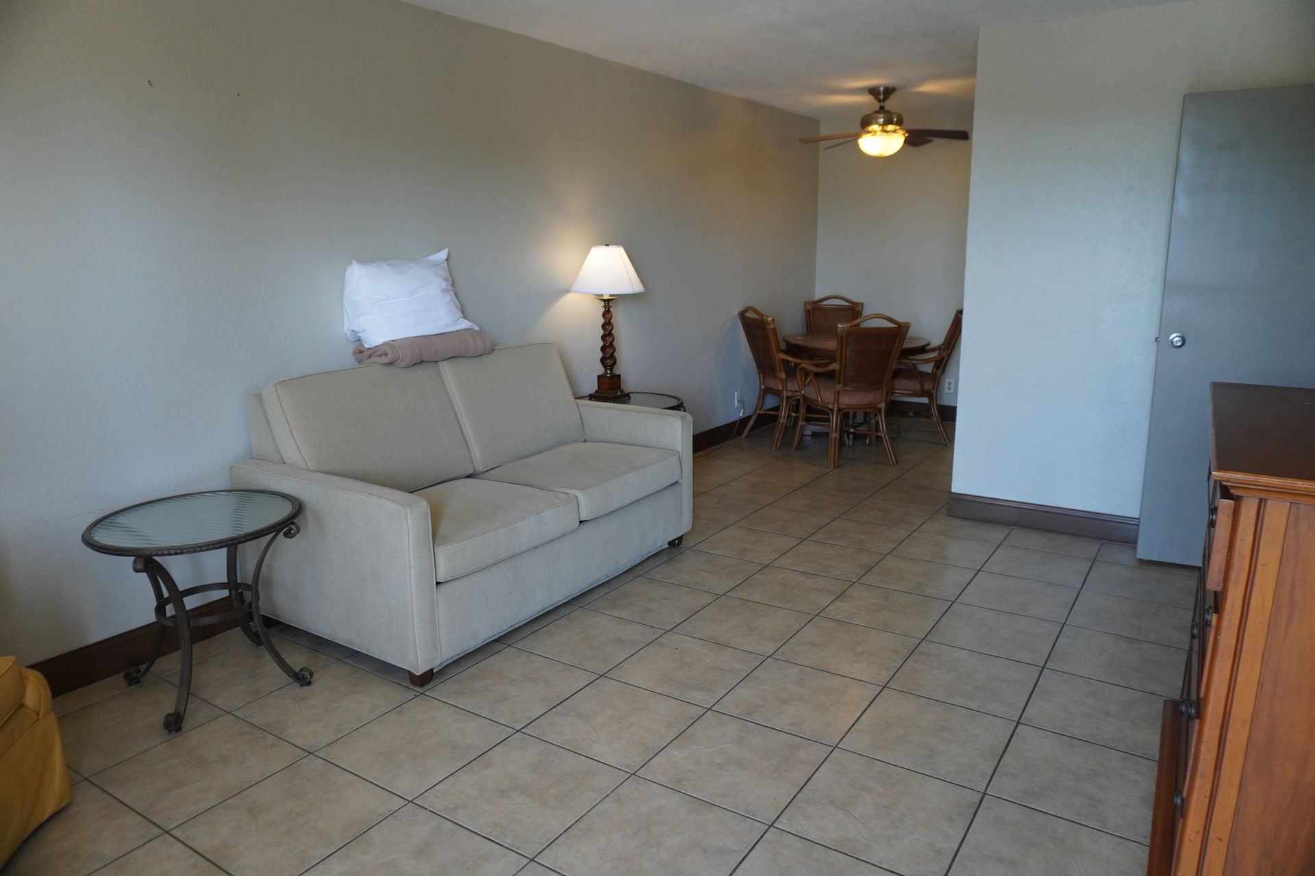Small living room with beige sofa, lamp, tiled floor, and dining table in the back