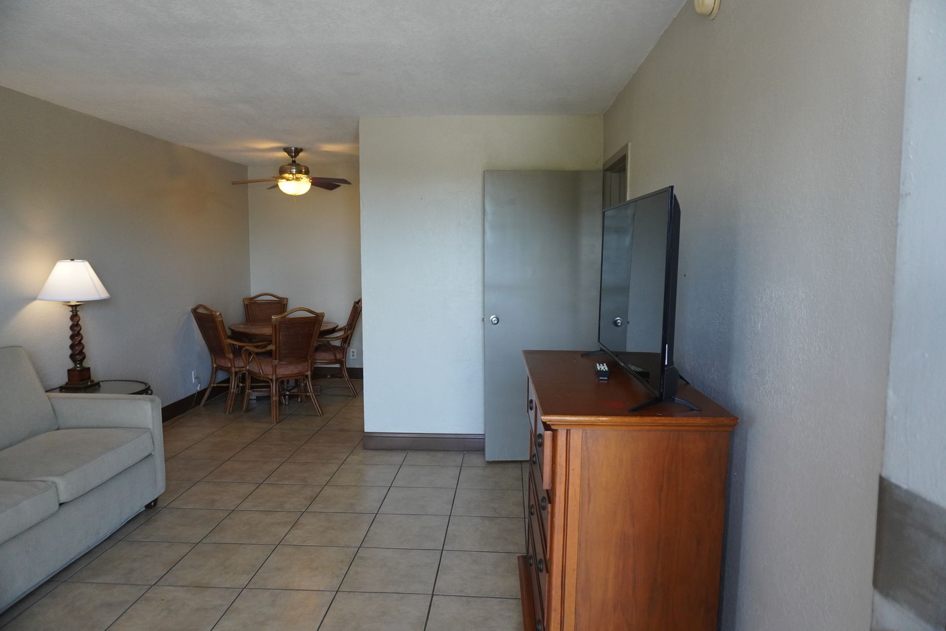 Living room with beige sofa, lamp, dining table, and TV stand on tiled floor