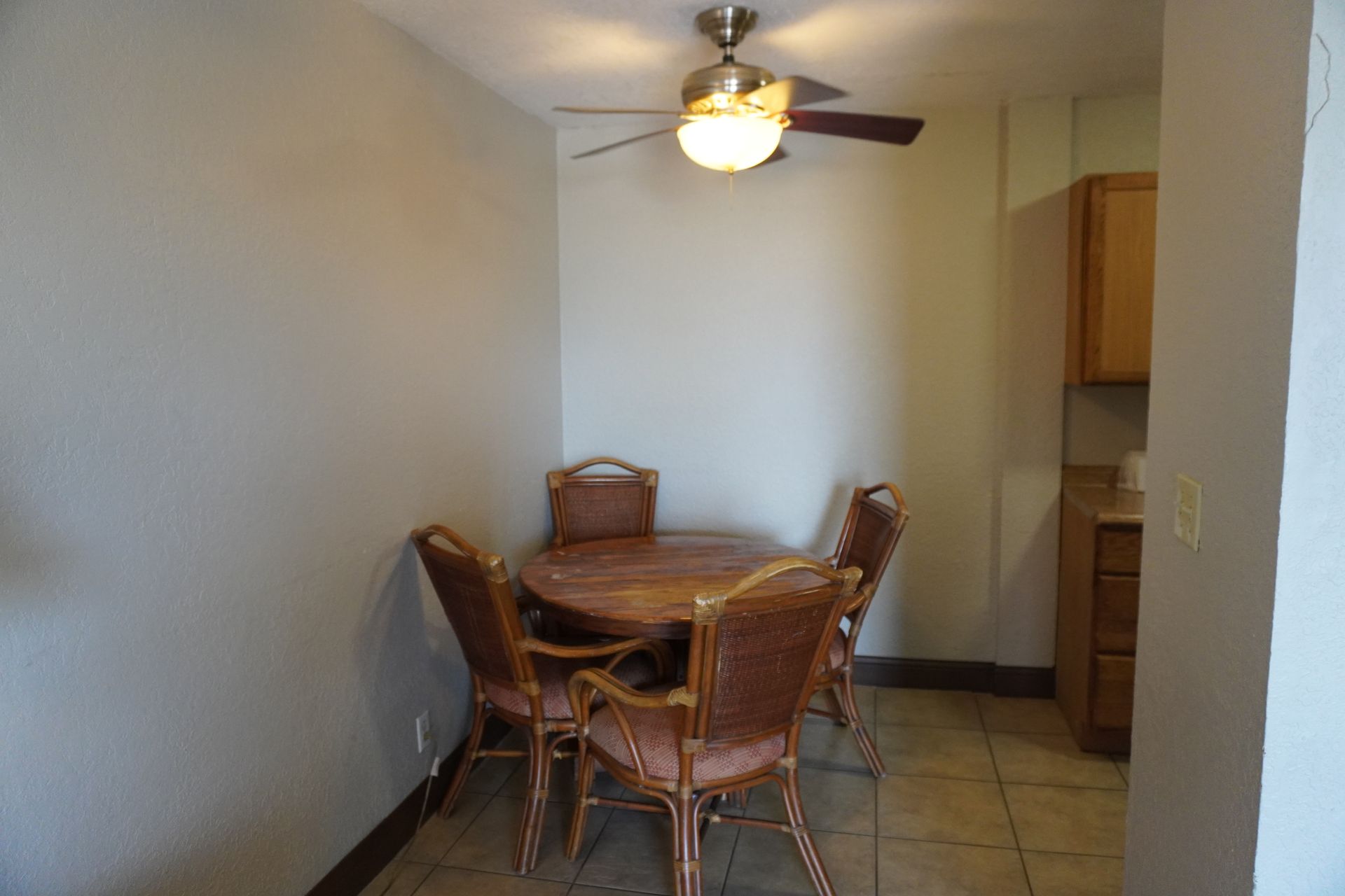 Small dining area with wicker table and chairs, ceiling fan, tiled floor, and kitchen cabinets nearby