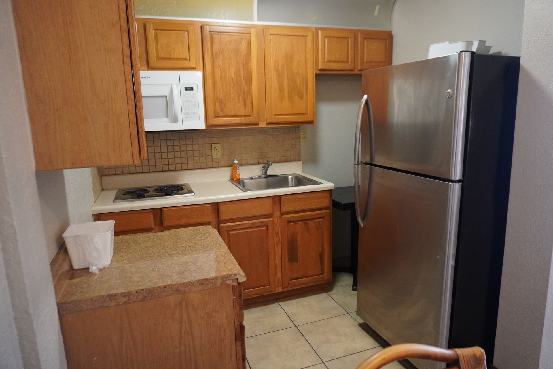 Small kitchen with wood cabinets, white microwave, and stainless steel refrigerator.