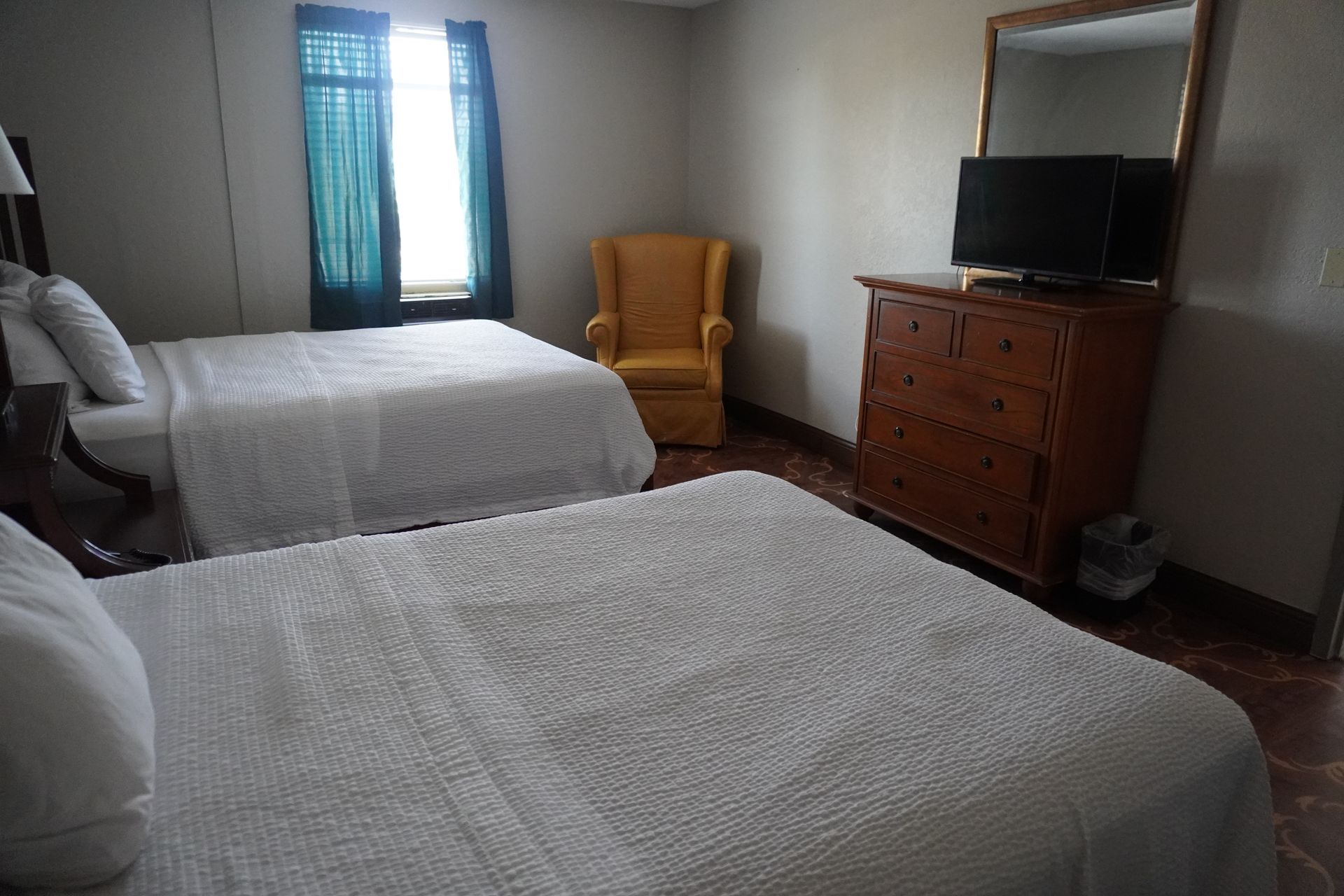 Bedroom with two beds, a yellow armchair, and a dresser with a TV near a window.