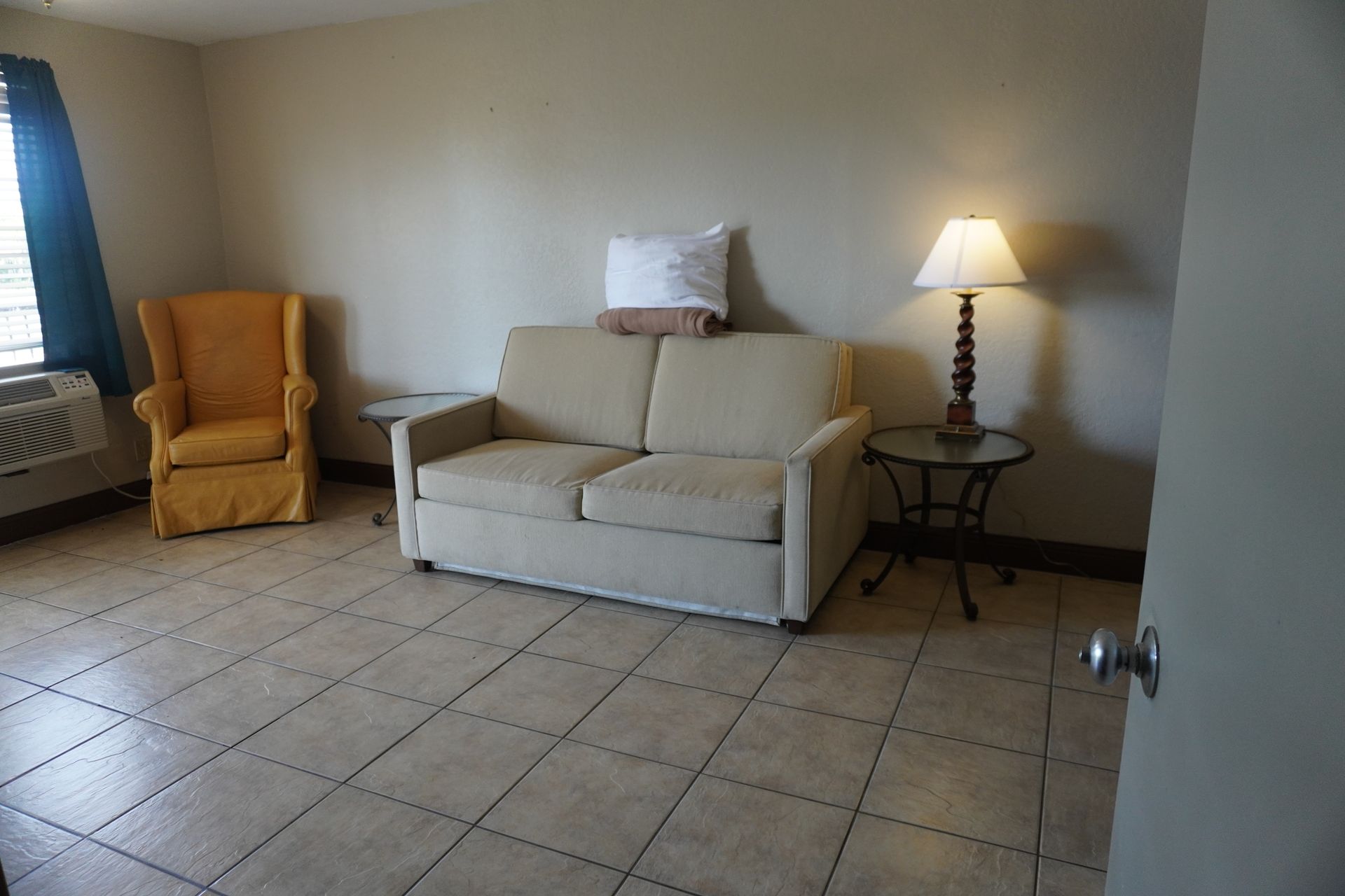 Cozy living room with beige sofa, yellow armchair, side lamp, and tiled floor.