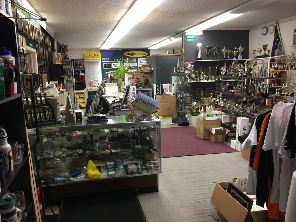 Inside a trophy shop with display cases, shelves of awards, and shirts on a rack.