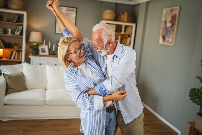 Two people dance in a cozy living room, smiling and embracing near a sofa.
