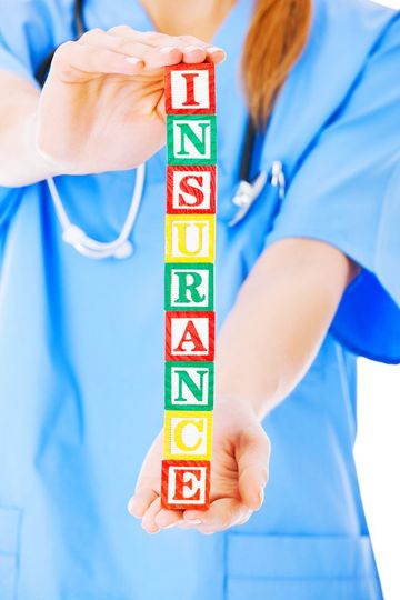 Healthcare worker holding letter blocks spelling “INSURANCE” with stethoscope in background