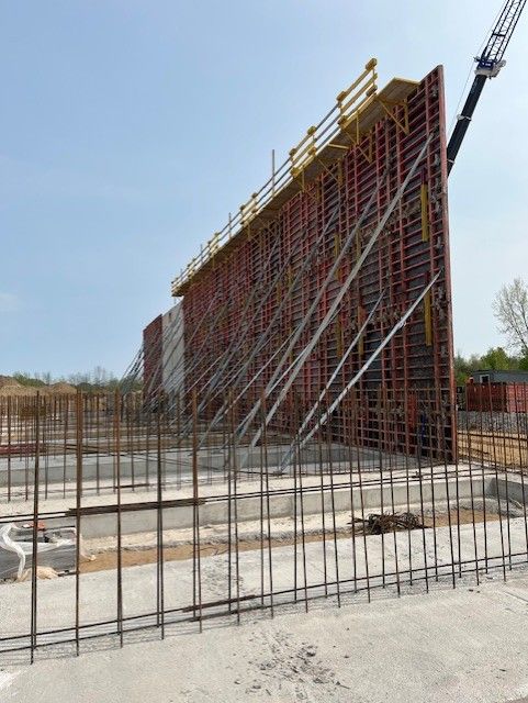 Construction site with red formwork wall and exposed rebar on a concrete slab under a clear sky