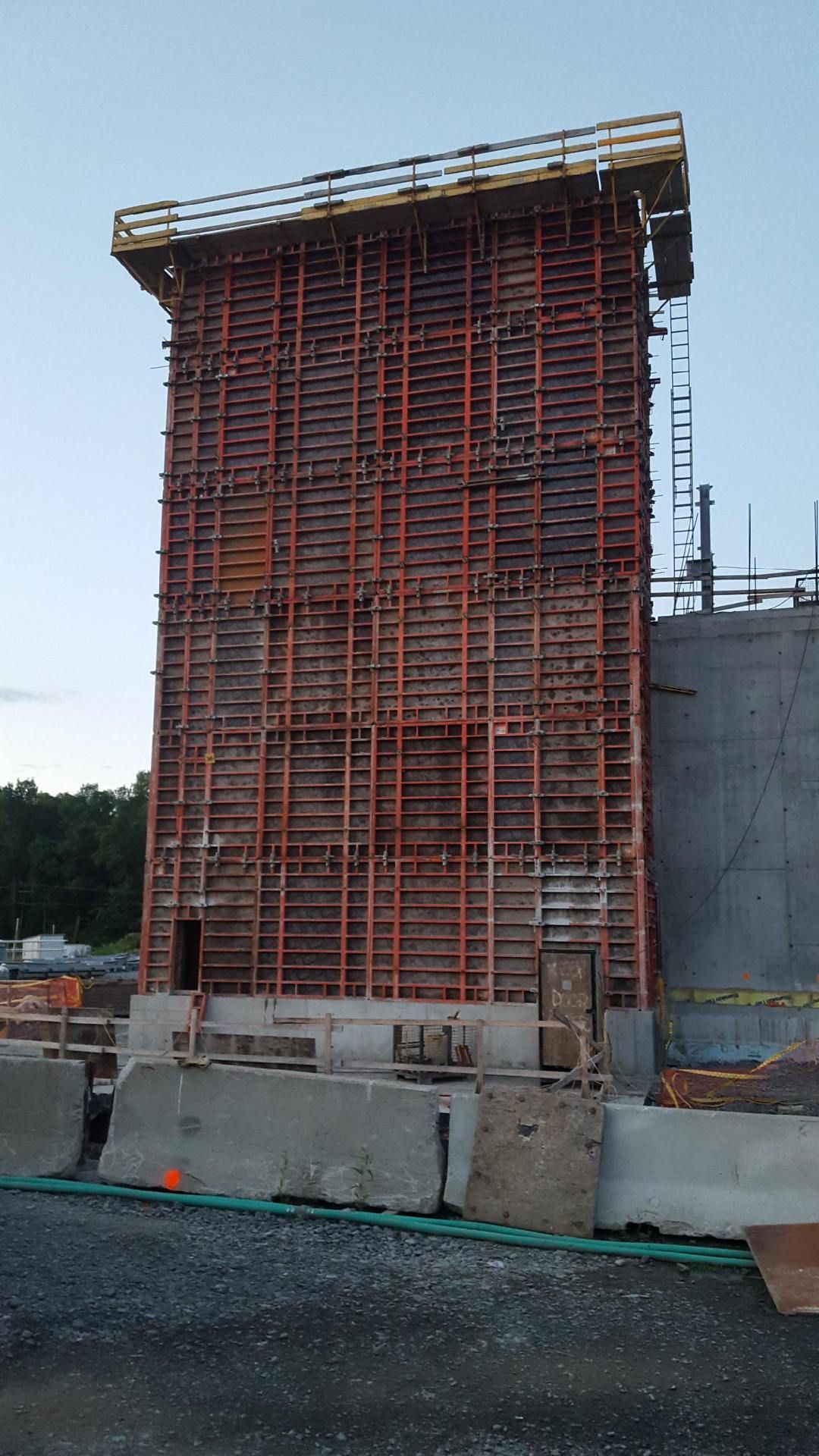 Tall red steel formwork at a construction site beside a concrete structure and barriers