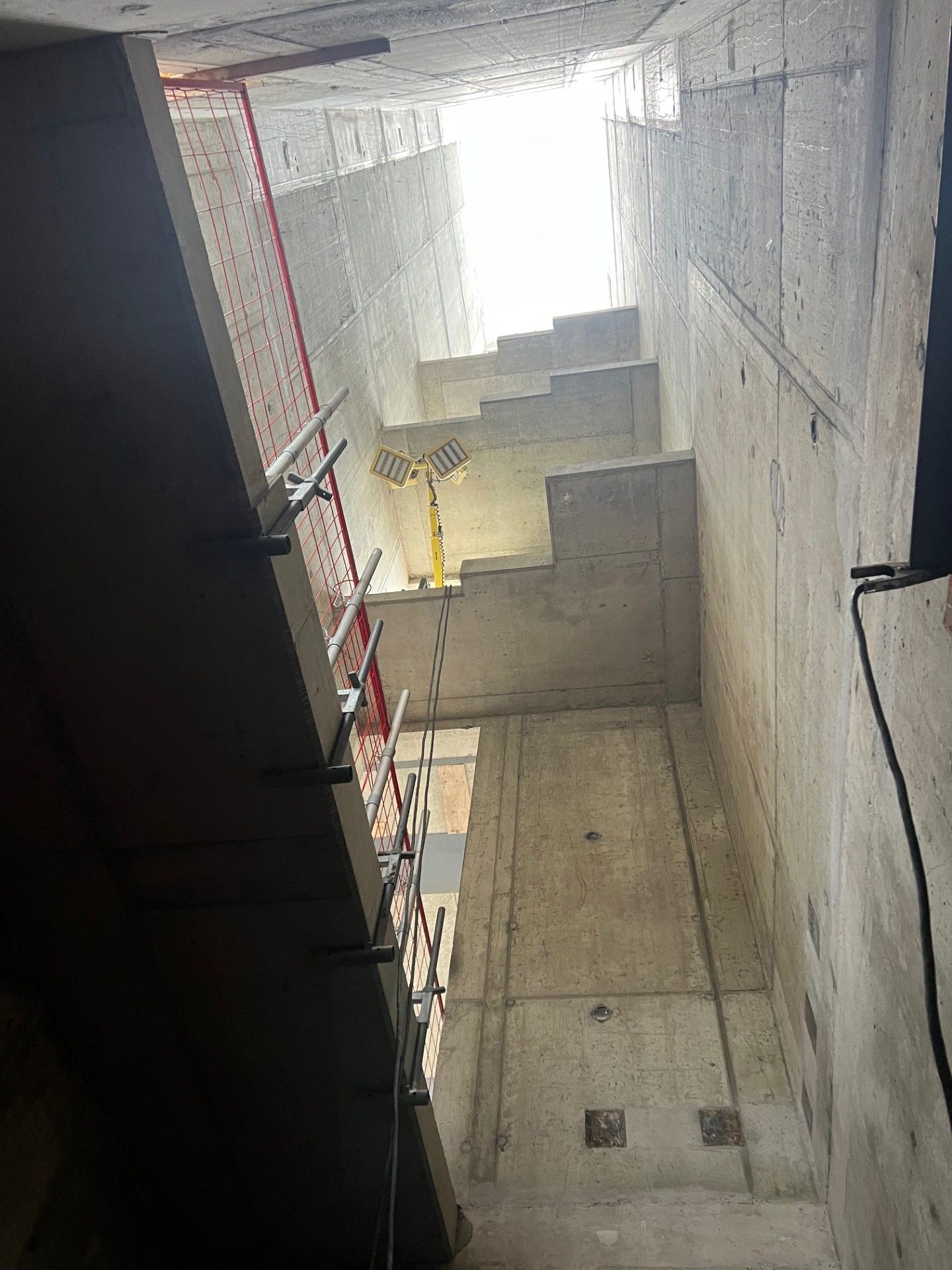 Vertical concrete stairwell with red handrails and bright light at the top opening