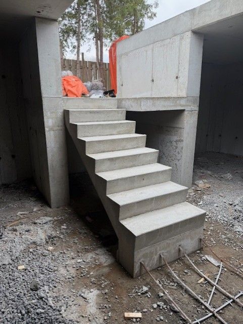 Concrete outdoor staircase under construction between unfinished gray walls and gravel ground.