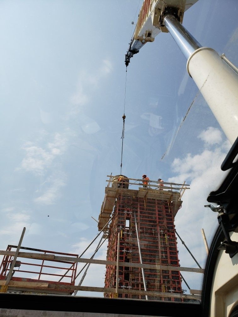 Construction workers atop a scaffold tower guiding concrete from a crane boom upward