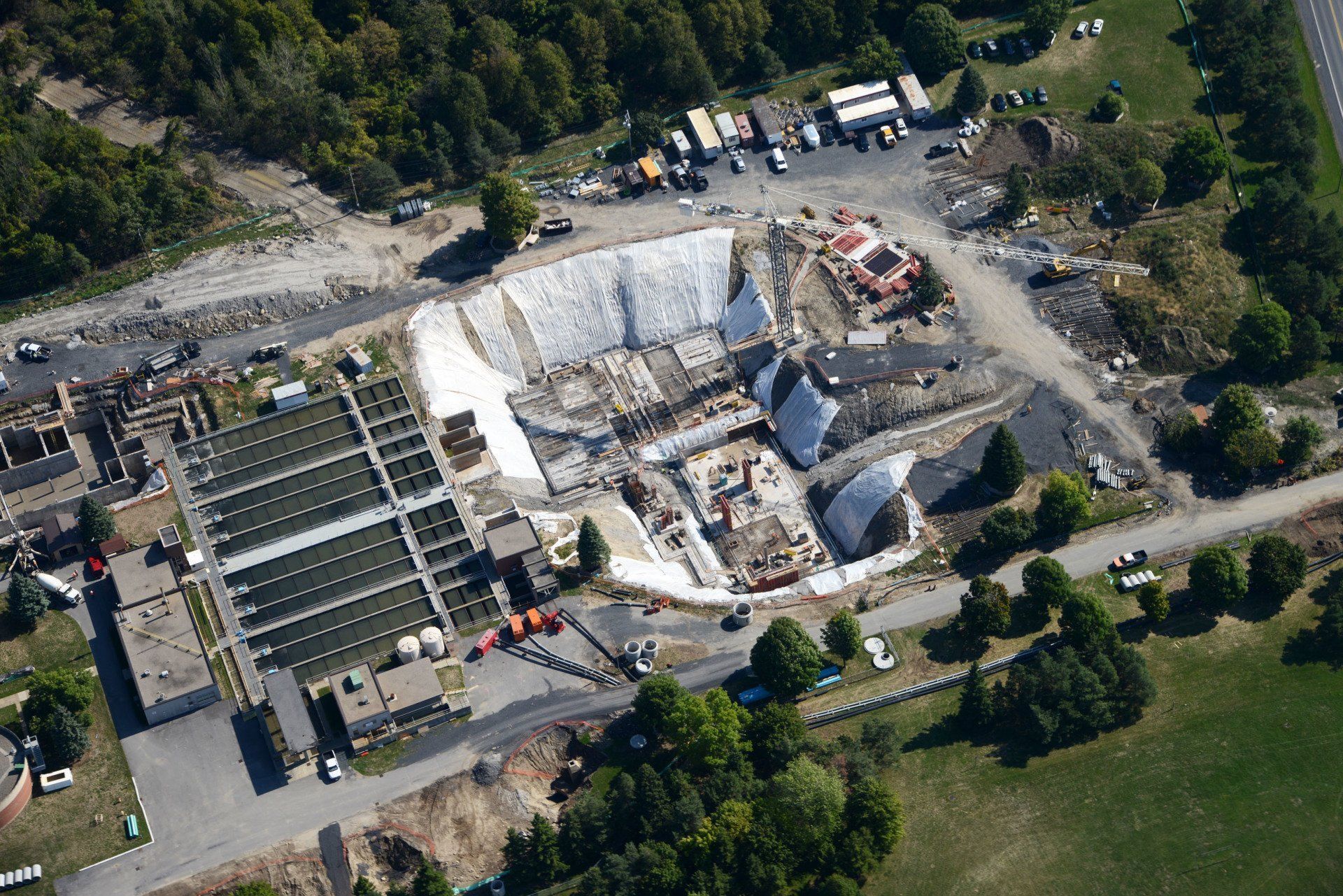 Aerial view of a damaged building site with heavy debris, parked vehicles, and surrounding trees.