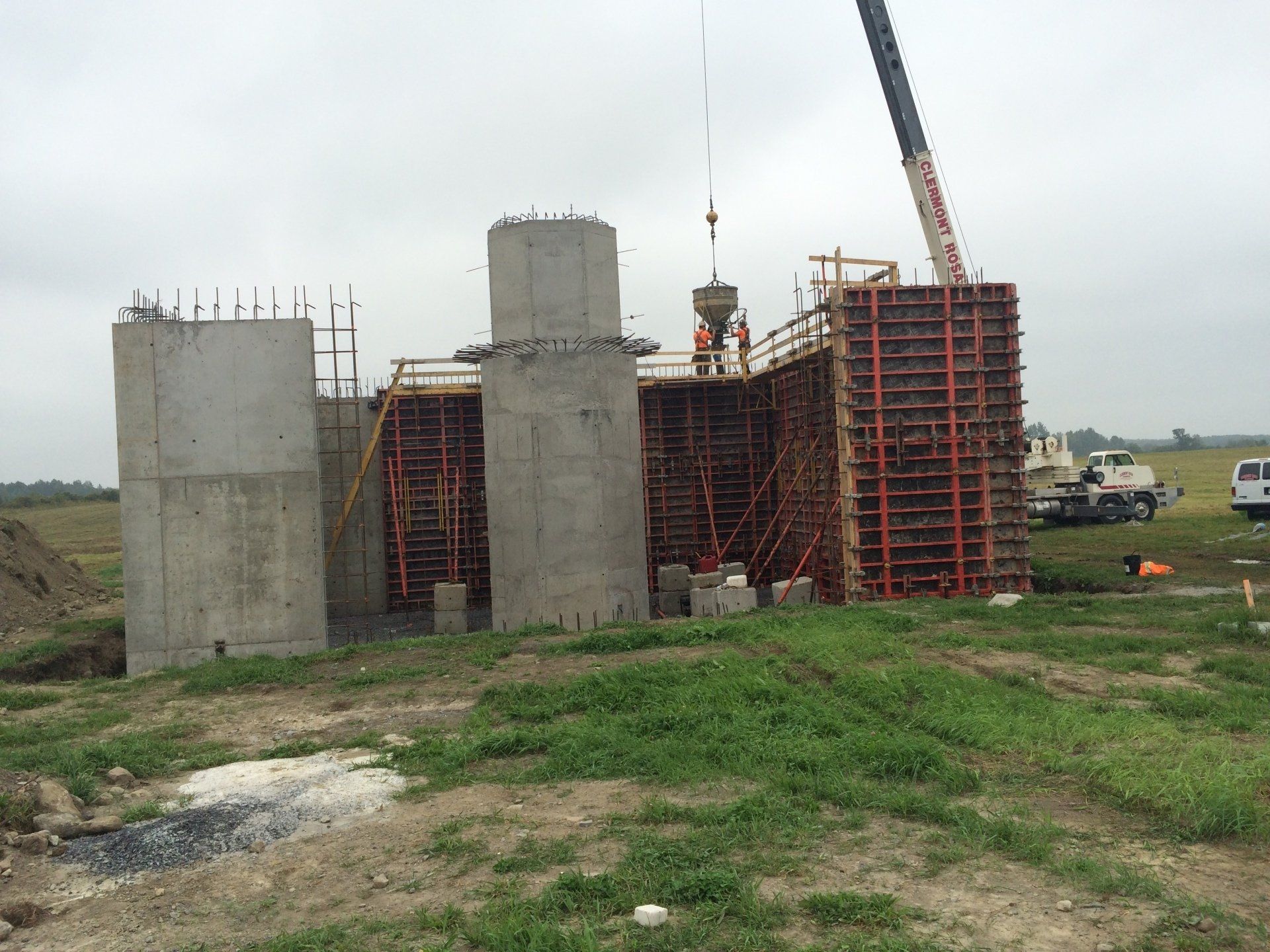Concrete bridge under construction with scaffolding and a crane on a grassy site