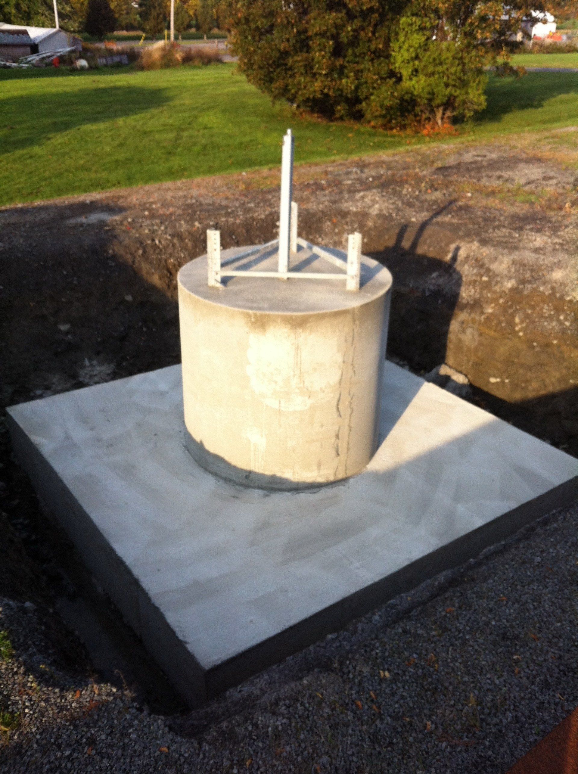Concrete cylindrical utility structure on a square slab in a grassy outdoor area