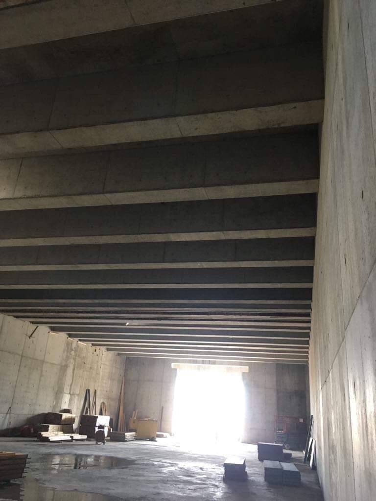 Empty unfinished concrete interior with beams and a bright opening at the far end