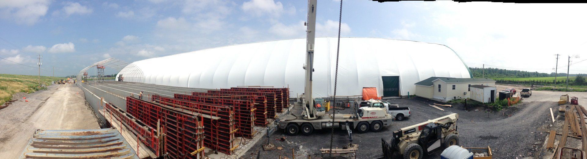 Construction site beside a large white dome building with cranes, vehicles, and stacked materials.
