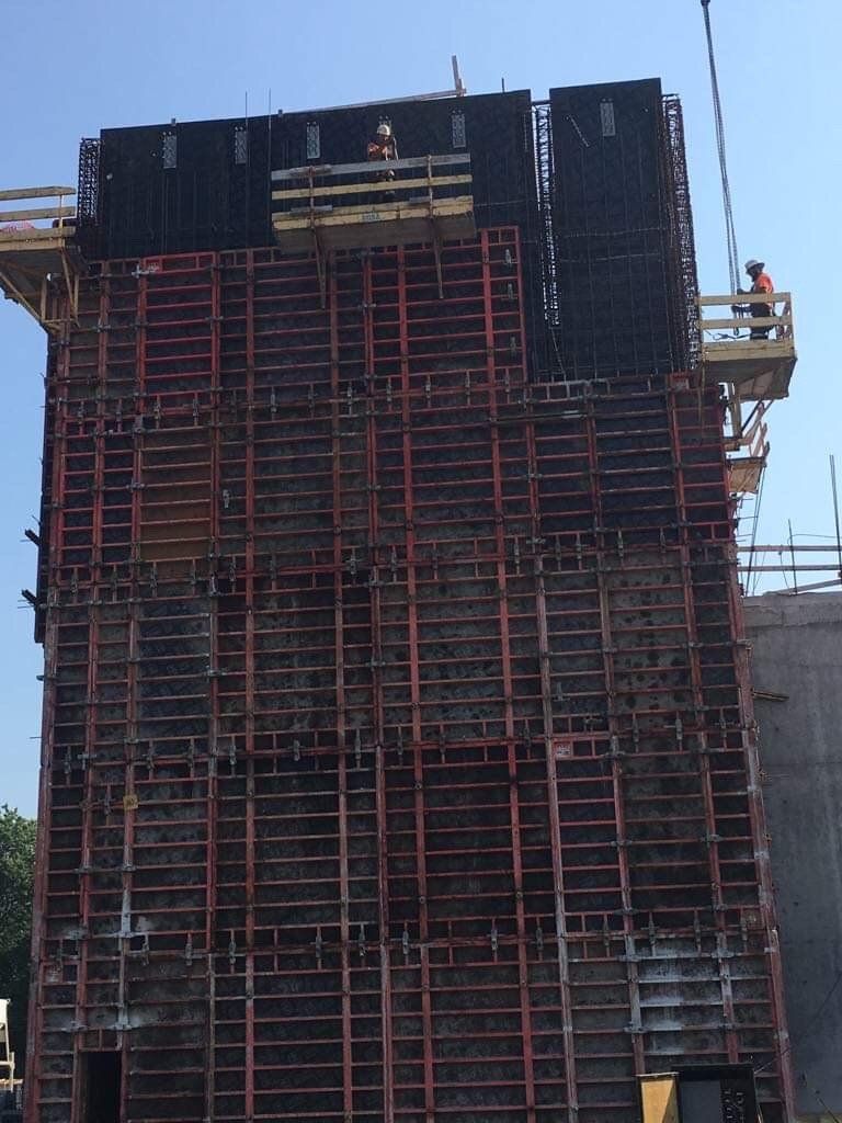 Tall concrete structure under construction with red scaffolding and workers on the right side