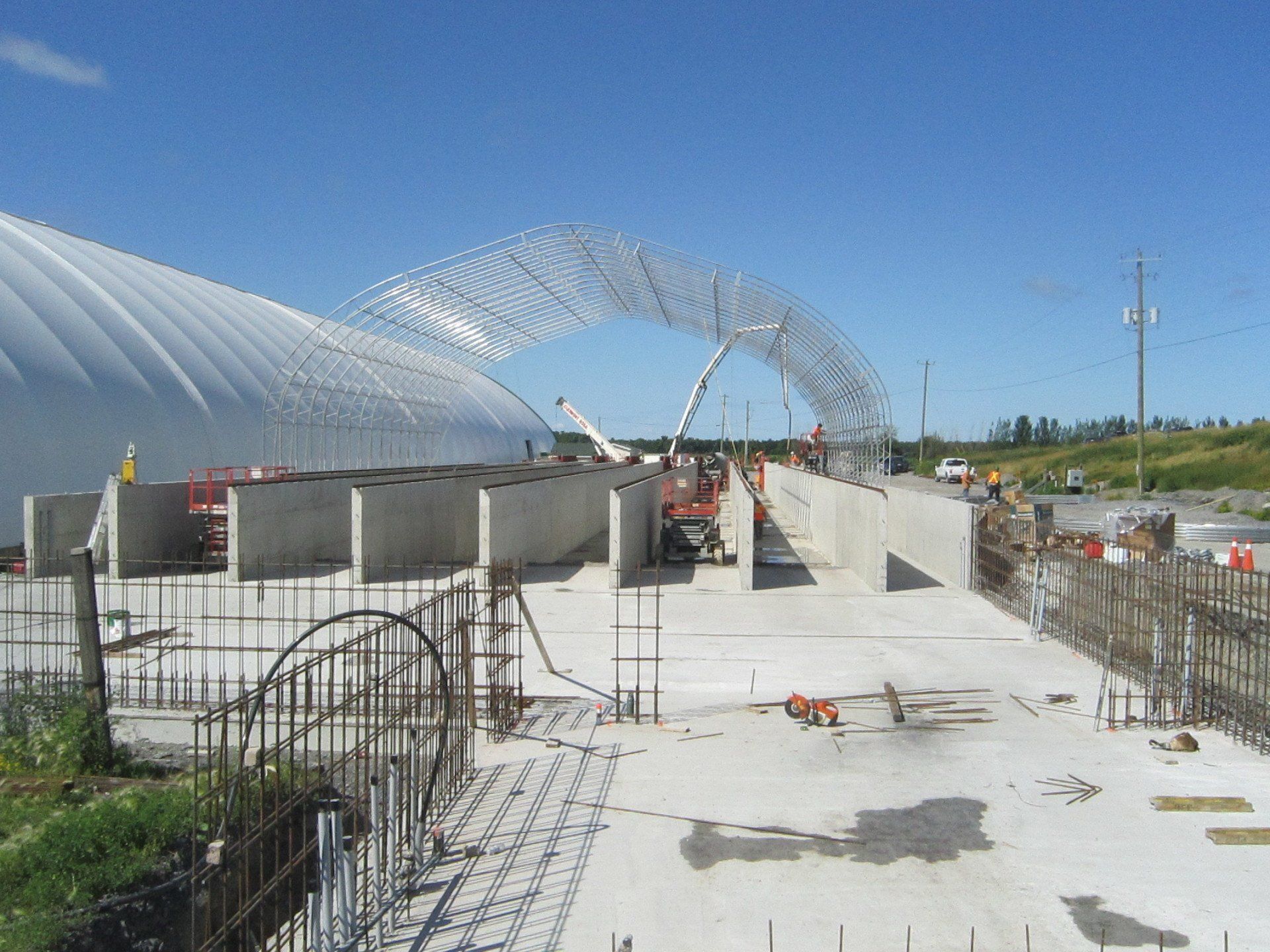 Construction site with curved steel arches over a concrete walkway under a clear blue sky