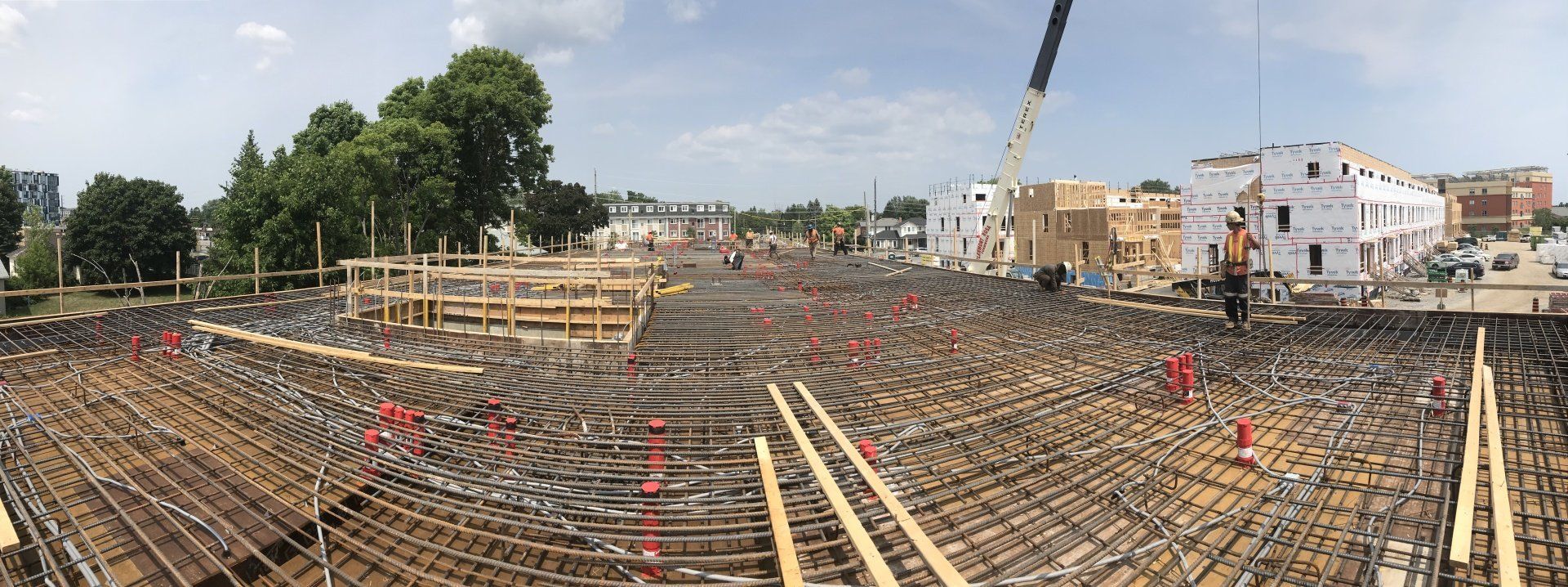 Construction site with curved rebar foundation, workers, and a crane in the background under a cloudy sky