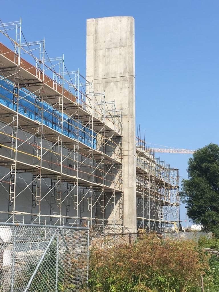Scaffolding around a concrete building under construction beside a tall concrete tower and blue sky