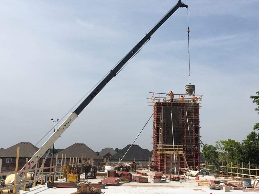 Crane lifting materials at a construction site beside a concrete structure under a clear sky