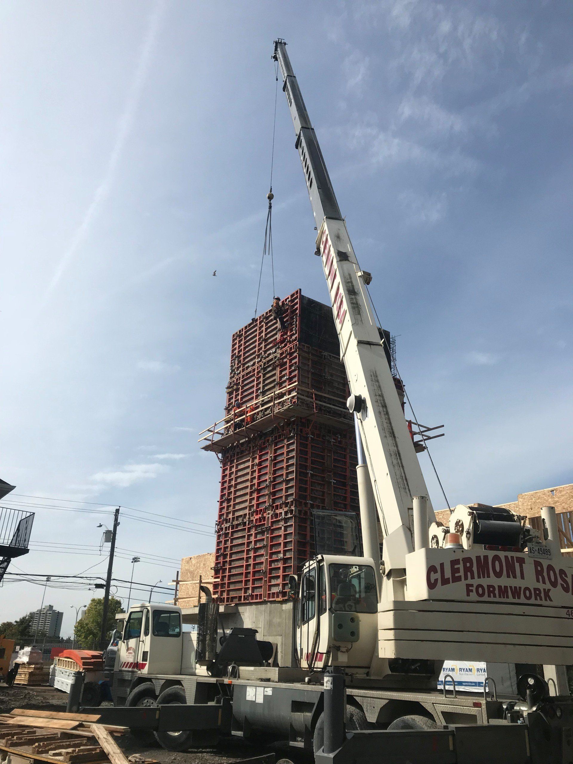 Crane lifting a large red formwork structure at a construction site under a clear sky