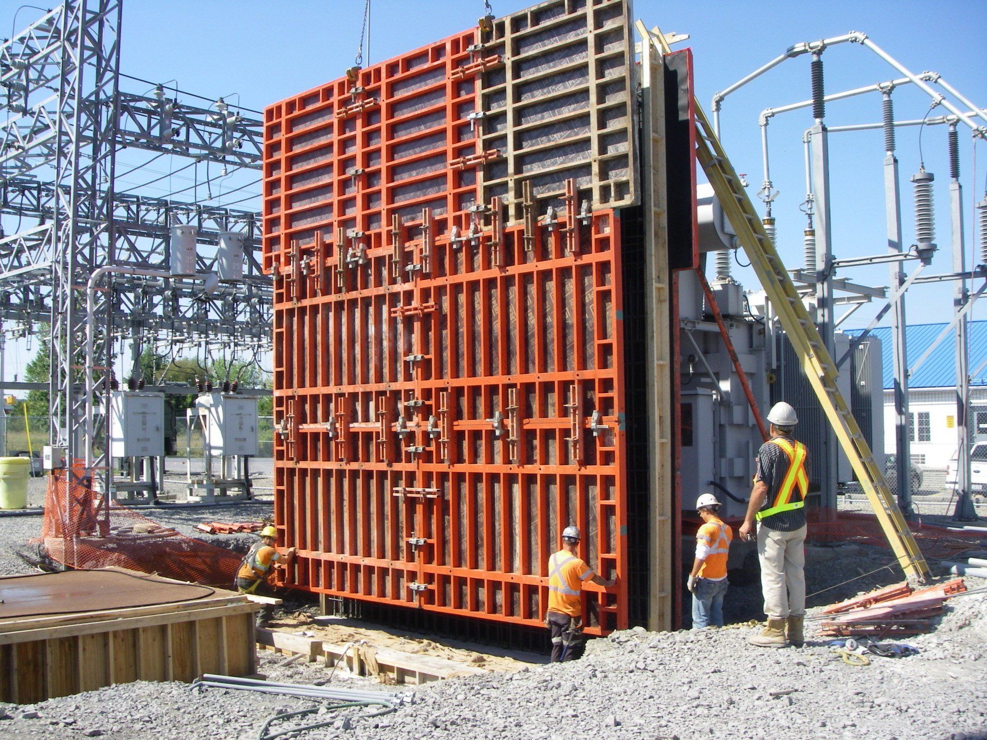Construction workers beside a large red formwork structure at an industrial site