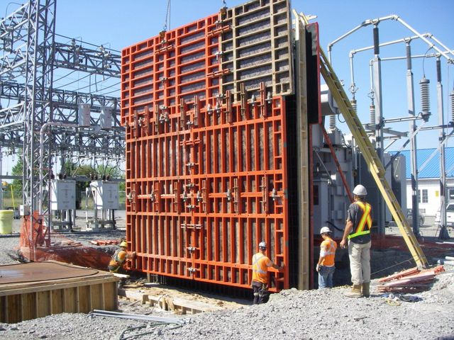 Construction workers beside a large red formwork structure at an industrial site