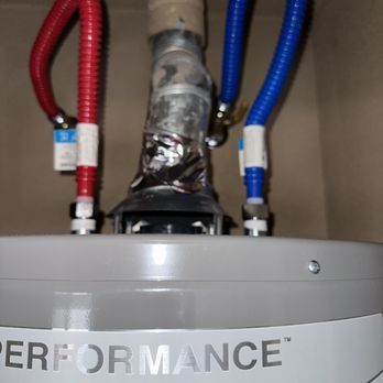 A close-up of a silver water heater with red and blue flexible water lines connected.