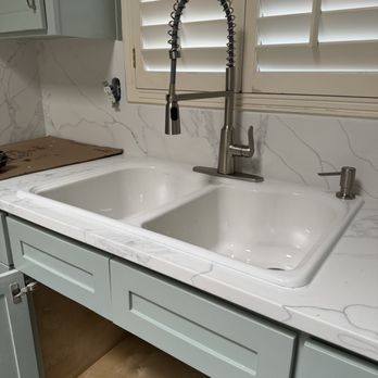 A kitchen sink with a marble-like countertop, a pull-down faucet, and light blue cabinets.