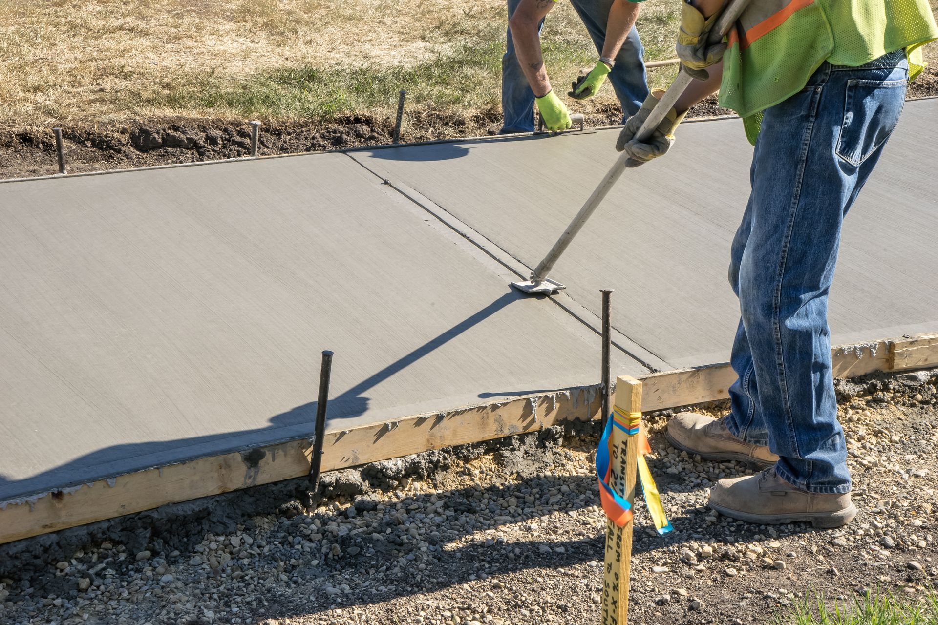 Two construction workers are working on a concrete sidewalk.