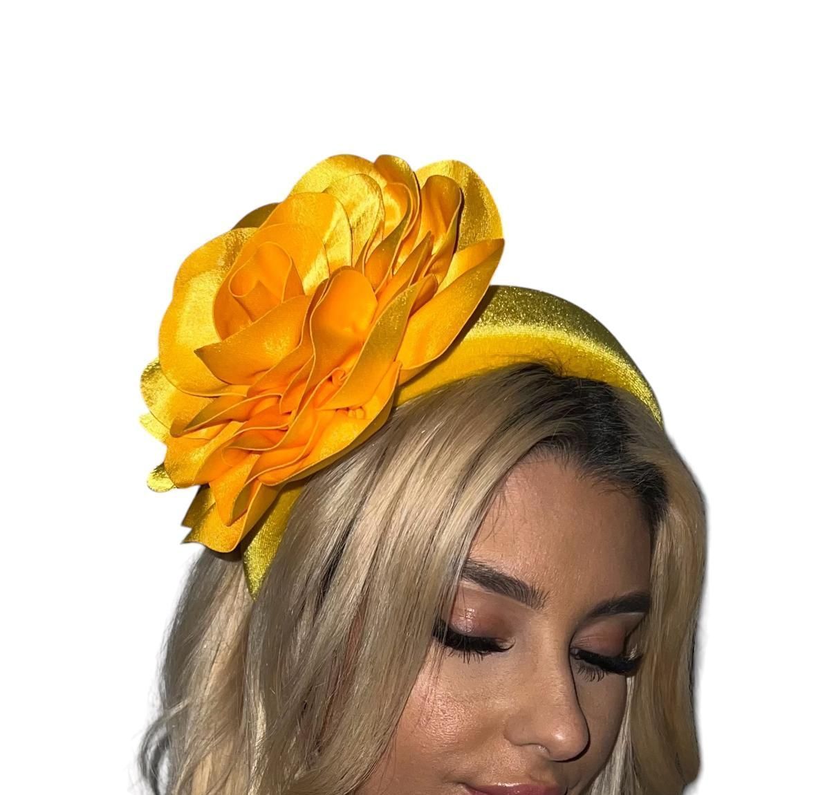 Woman wearing a large yellow flower headpiece and blonde hair, eyes closed against a white background
